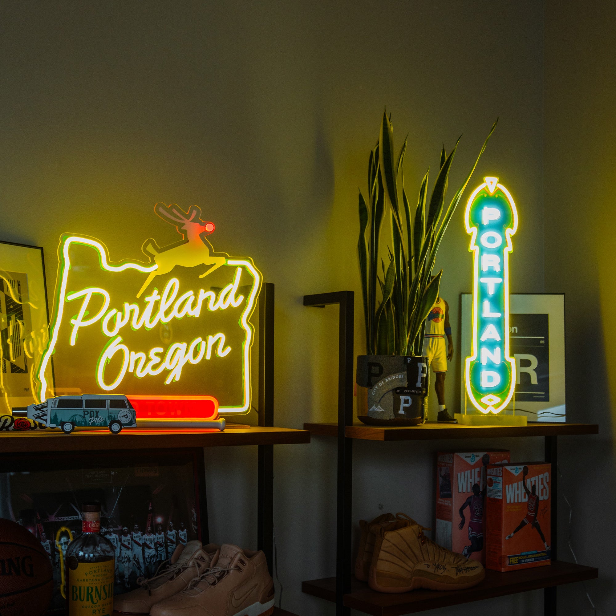 A brightly lit room features shelves displaying various items and neon signs. An LED Marquee Sign outlines the shape of Oregon and reads "Portland Oregon" in yellow and red, while another vertical custom LED sign displays "Portland" in teal and white. Decorative items and plants are also visible, enhancing the energy-efficient ambiance.