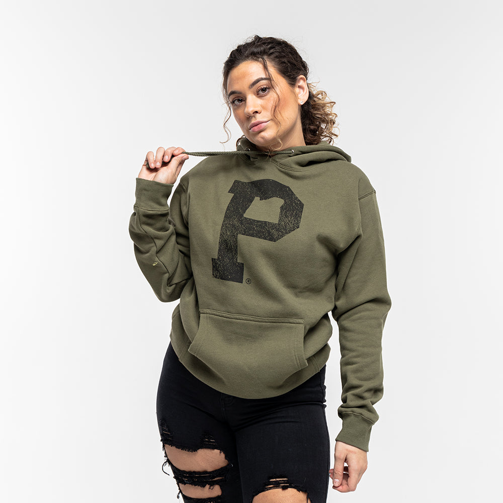 A person with curly hair is wearing a Soft-Blend "P" Hoodie in olive, featuring a large black "P" on the front. They are holding one of the hoodie strings in their right hand and sporting distressed black jeans. The background is plain white.