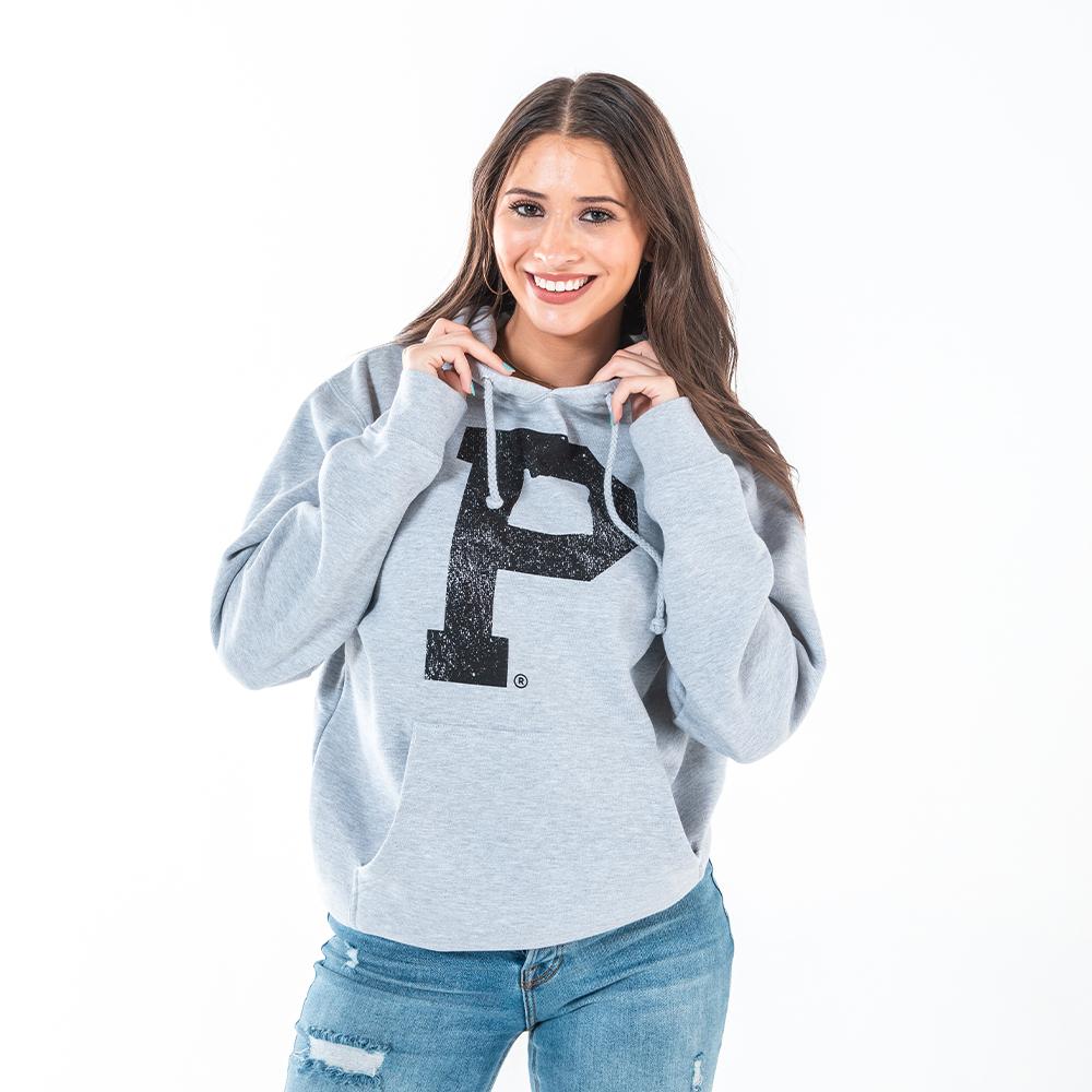 A smiling woman with long brown hair, dressed in a Soft-Blend "P" Hoodie - Grey featuring a large black letter "P" on the front, holds the drawstrings of her hoodie. She is also wearing distressed blue jeans against a white background.