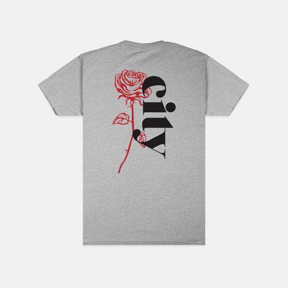 The Soft-Blend Rose City "P" Tee - Grey is a unisex cotton polyester shirt featuring a large red rose and the word "City" in black, stylishly arranged on the back. The design is centered and extends from the top to the bottom of the shirt, delivered in sustainable packaging.