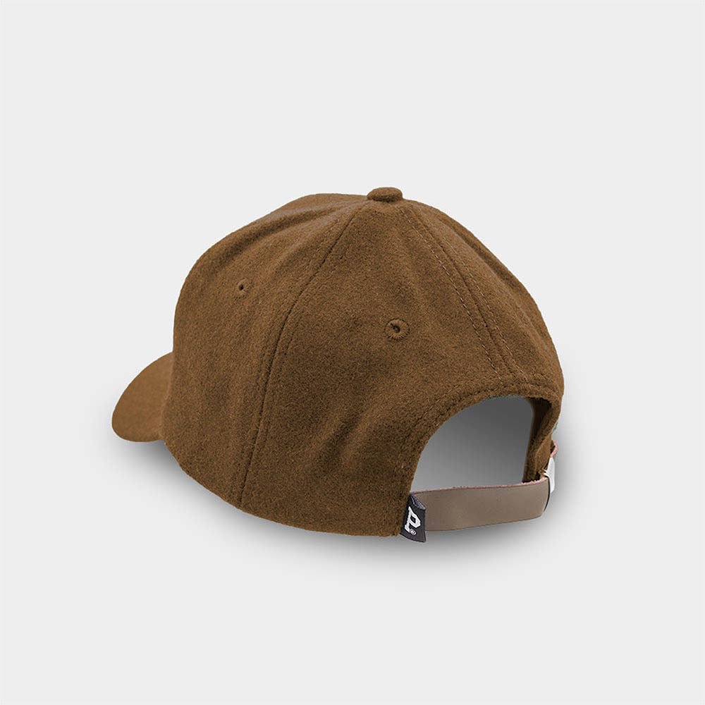 The Portland "P" Cap - Brown is displayed from the back, showcasing its curved brim and a fabric strap with a metal buckle for adjustments. A small black tag with a white logo is positioned near the fastening. The cap is set against an off-white background.