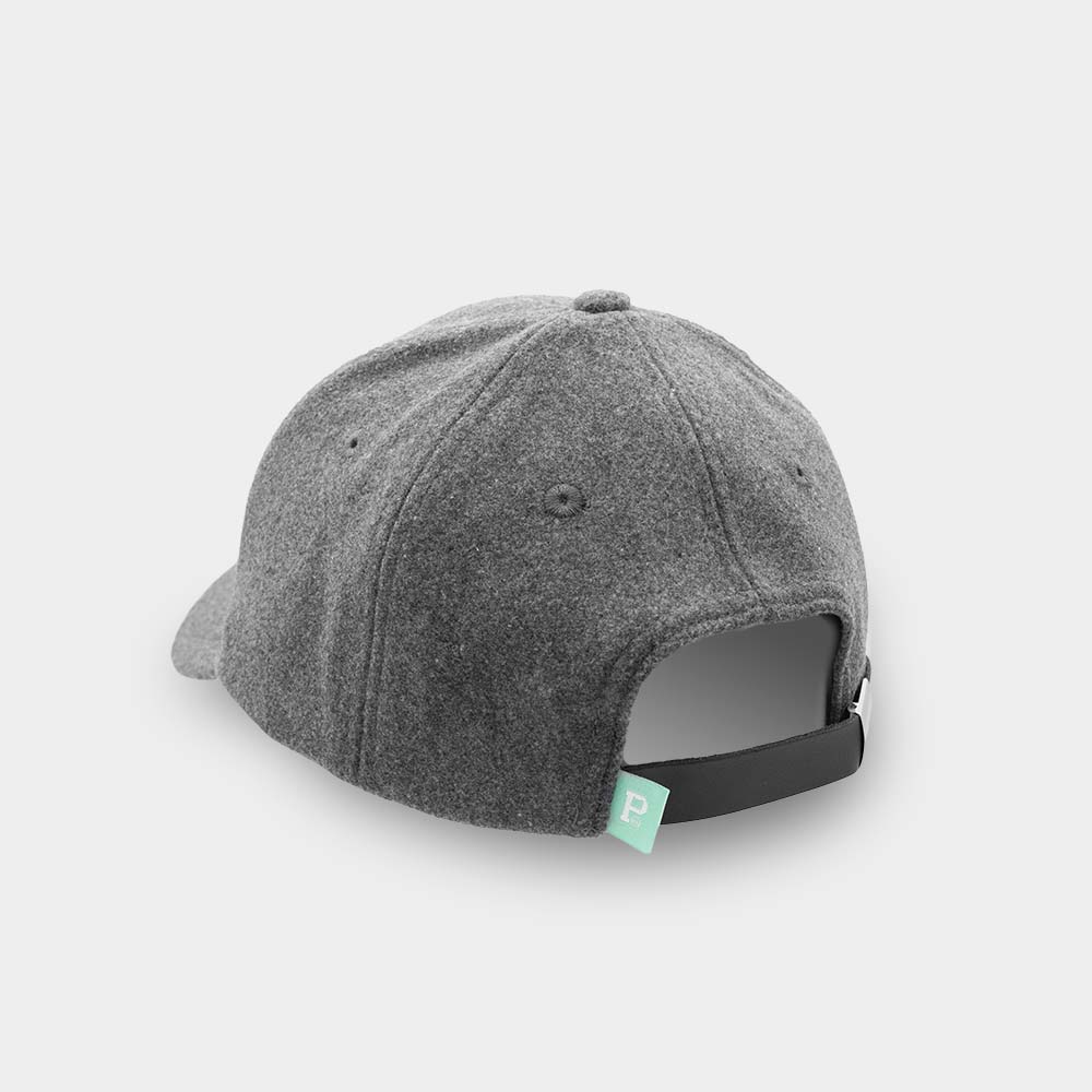 The Portland "P" Cap - Dark Grey is displayed from the back, showcasing an adjustable black strap with a metallic clasp. A small green tag with a white "P" is attached to the strap, indicating that this is a SHELL PRODUCT. The background is plain and light gray.