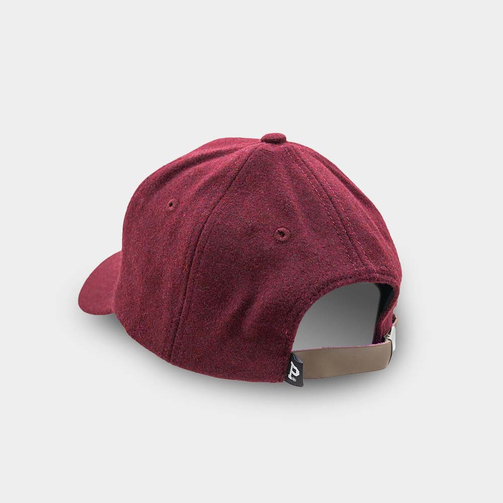 The maroon Portland "P" Cap is shown from the back, featuring a curved brim and an adjustable beige strap with a metal buckle. Eyelets provide ventilation, and there is a small black tag with a white logo attached near the strap.