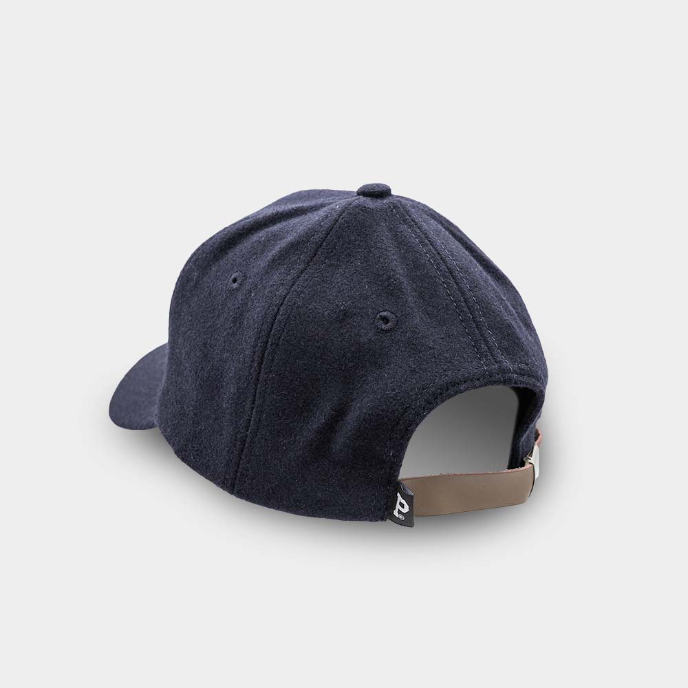 The Portland "P" Cap - Navy, depicted on a light gray background, is shown from the back. It features a dark blue shell with traditional panel stitching and an eyelet on each panel. The cap includes a brown adjustable strap with a small black tag near the closure.