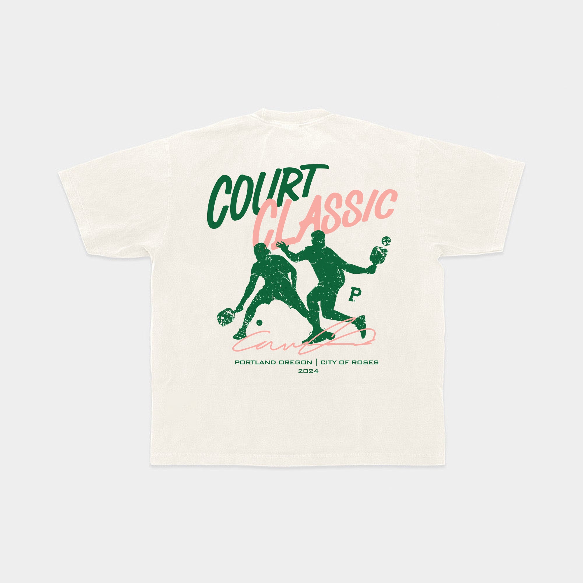 Introducing the All-American Court Classic Tee: a beige 100% cotton t-shirt showcasing a dynamic green and pink design on the back. The graphic features two illustrated players in an intense basketball game, with "Court Classic" above them and "Portland Oregon | City of Roses 2024" below. Packaged sustainably for an eco-friendly touch.