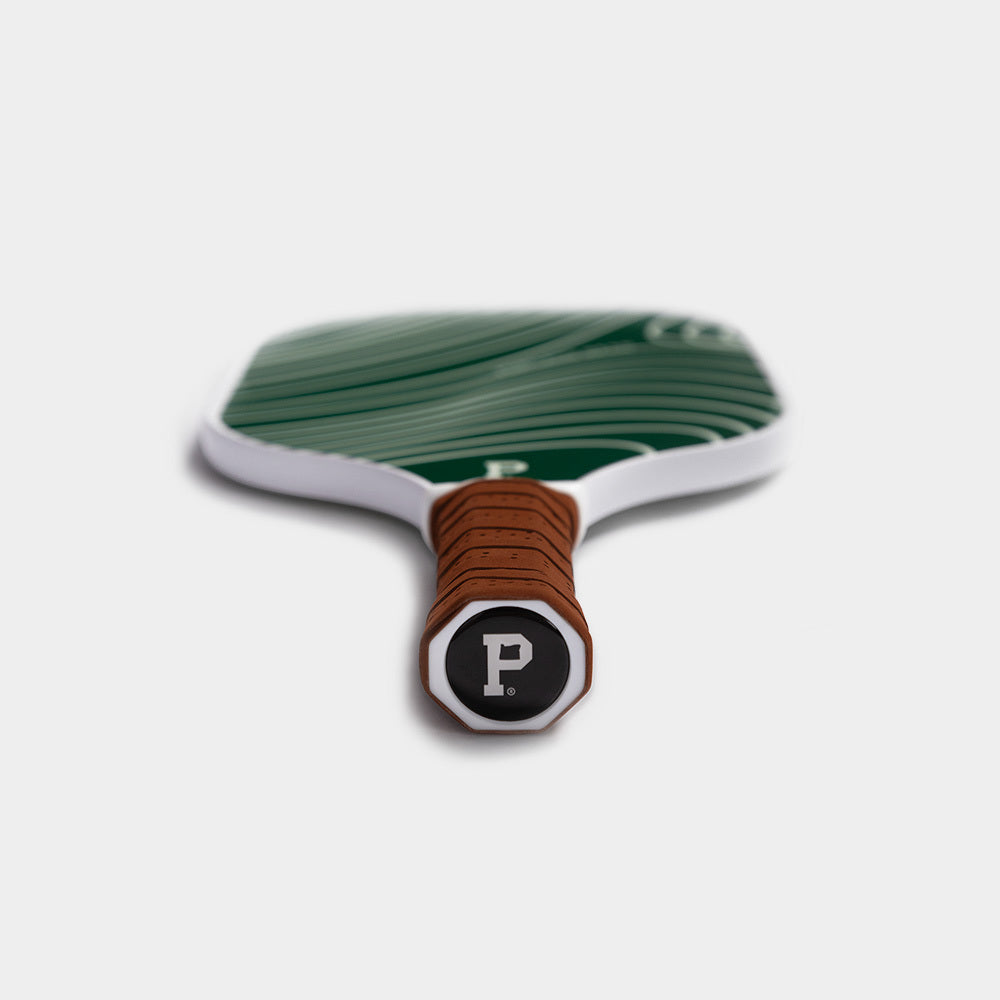 A close-up image of the limited edition Pickleball Paddle with a green surface featuring curved white lines. The handle is wrapped in brown material and ends with a black cap displaying a white letter "P" inside a white circle, reminiscent of Portland Gear's signature style. The paddle is shown from the handle's end.