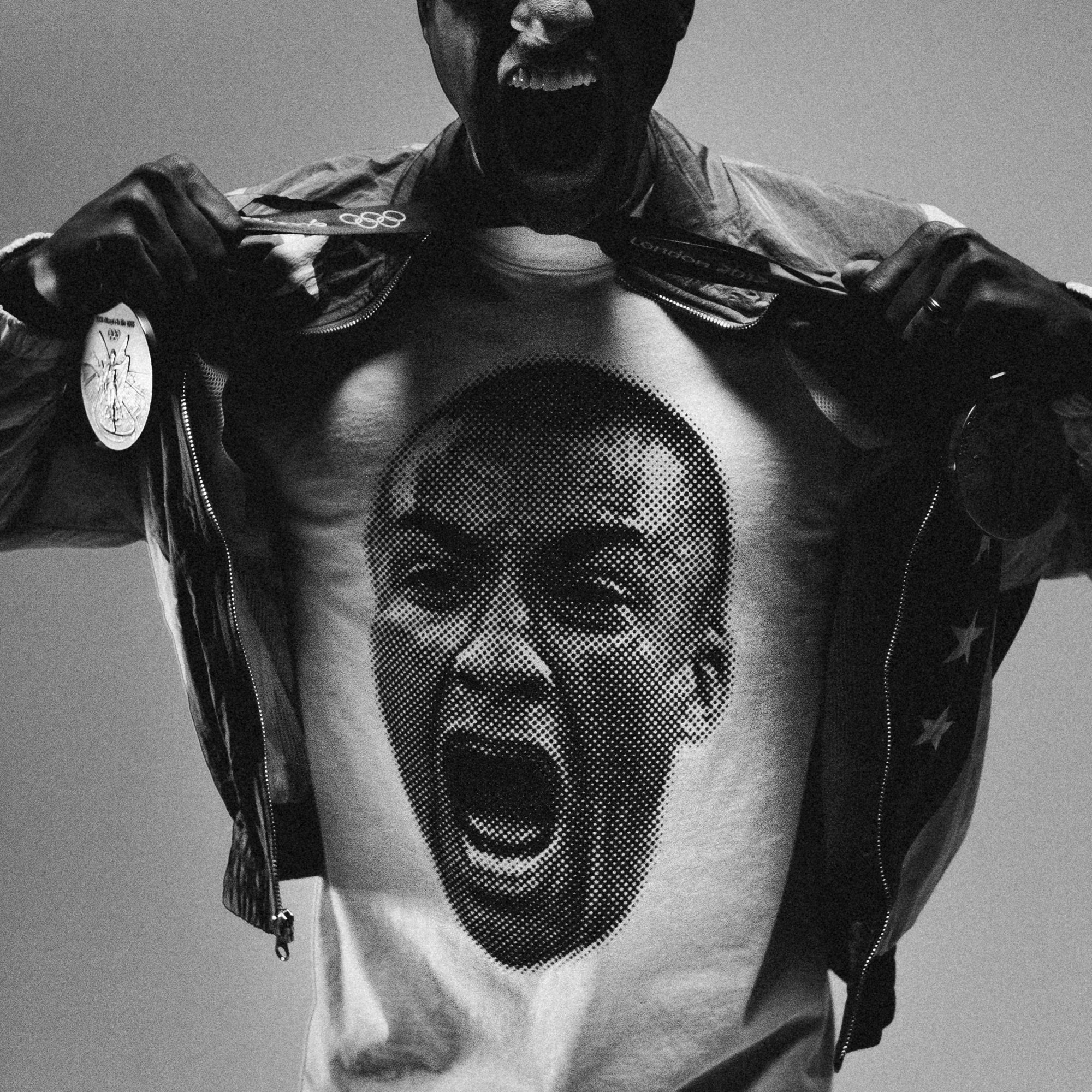 A black and white photo shows a person wearing a jacket and pulling it open to reveal the All-American Ashton Eaton Oversized Tee, featuring a large, detailed image of a shouting face printed on it. The raw intensity in their expression feels as powerful as the drive of the greatest athlete, possibly inspired by the 2024 Olympics.