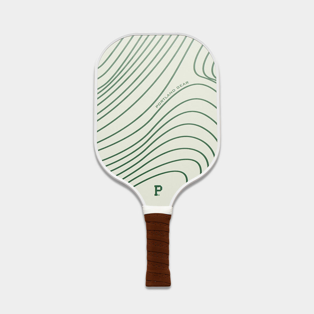 An image of the Pickleball Paddle, a limited edition model with a green and white design featuring wavy lines. The paddle has a white frame, a brown grip handle, and is accented with a small "P" logo at the bottom of the paddle face along with text that reads "Portland Gear" along the side.